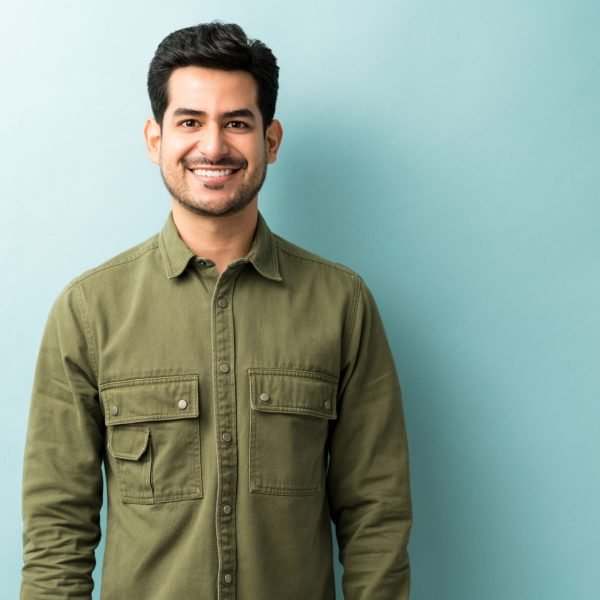 Handsome smiling man wearing green shirt standing against blue background
